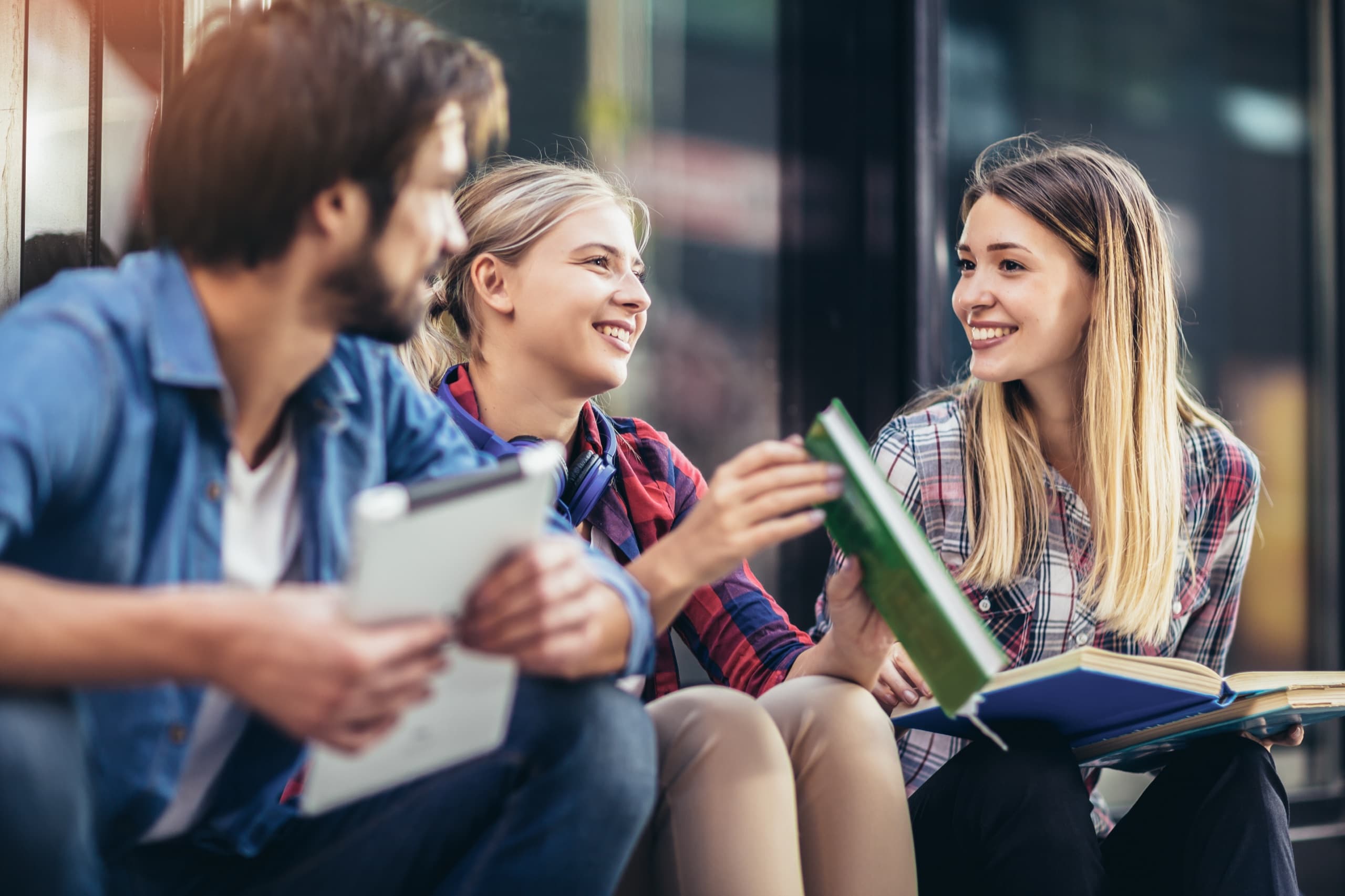Three students talking with books and a tablet